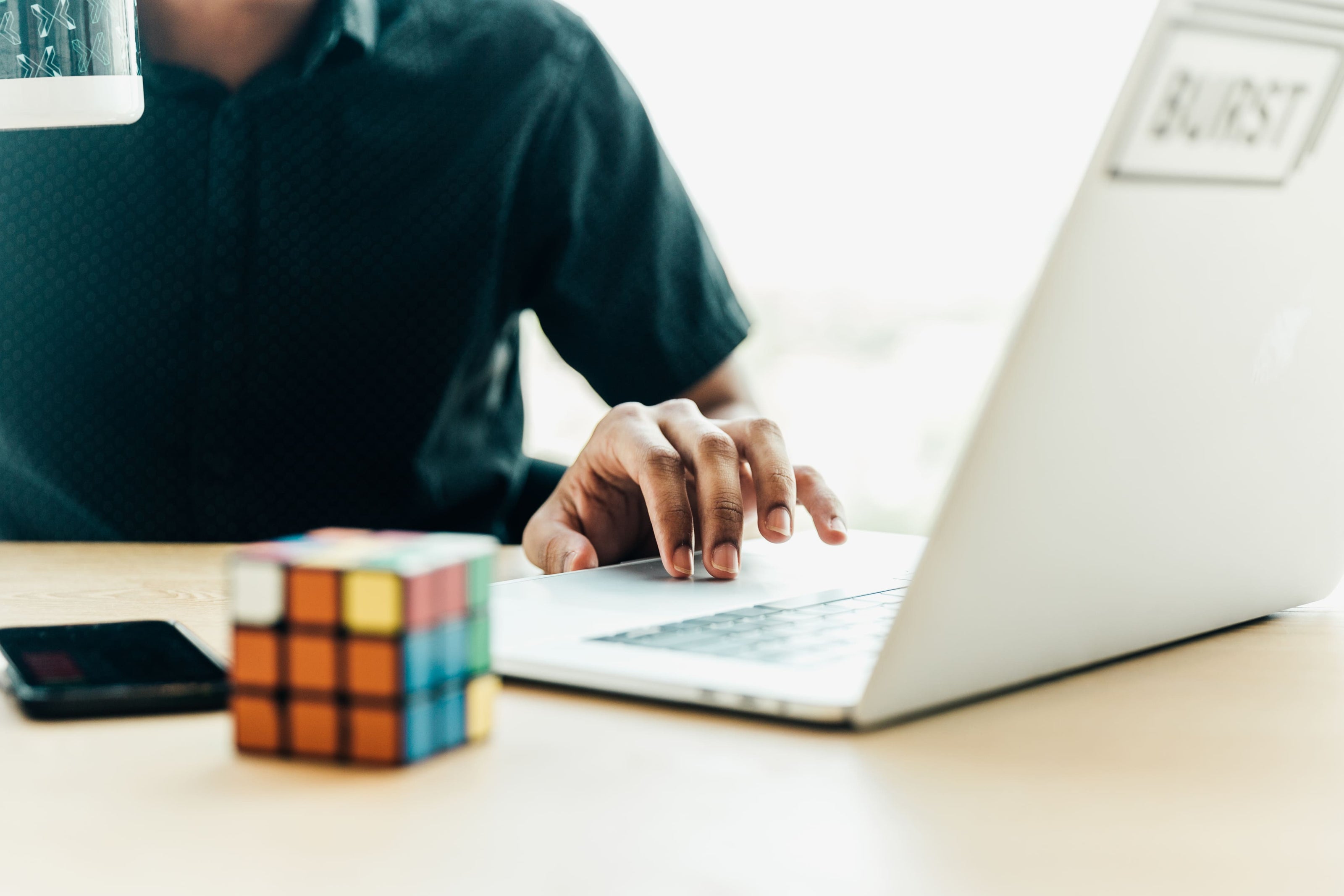 Person working on a laptop with a Rubik's cube on a desk