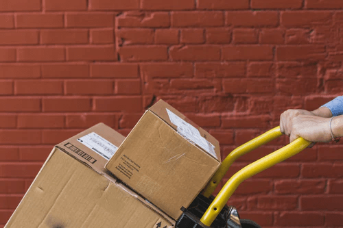 Person pushing a hand truck loaded with cardboard boxes